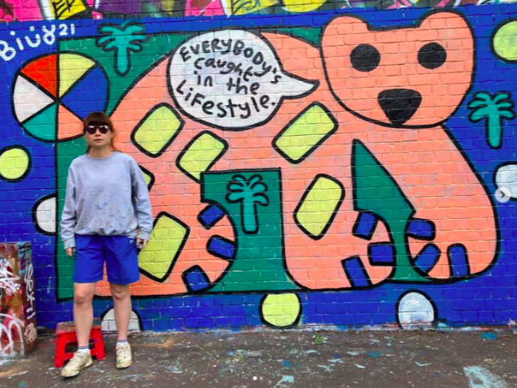 Billy Colours stands in front of one of their murals.