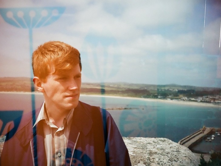 Photograph of Callum Perrin in front of the sea, it is a sunny day.