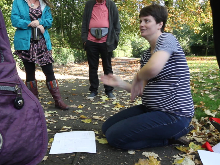 Claire Weetman knelt down in a park speaking to a group of people stood up around her.