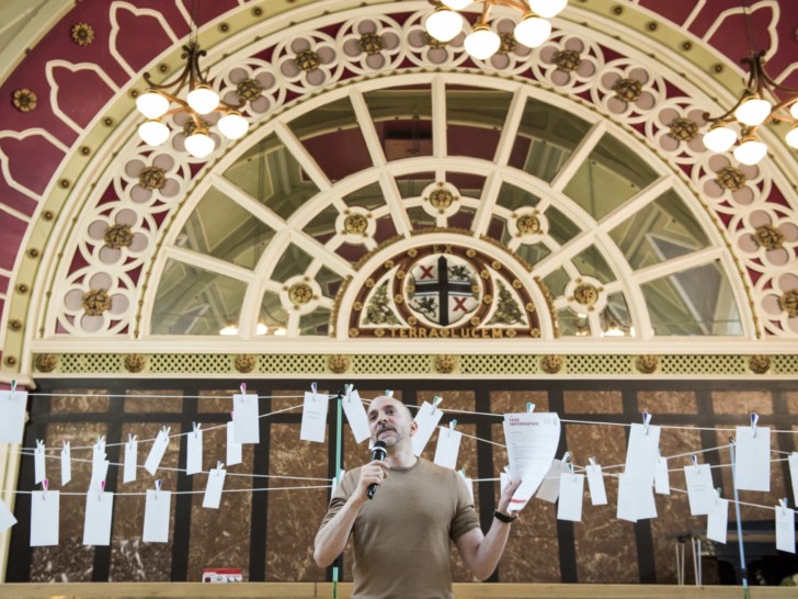 Joshua stood in front of decorative arch in St Helens town hall holding a sheet of paper reading 'Task Information'.