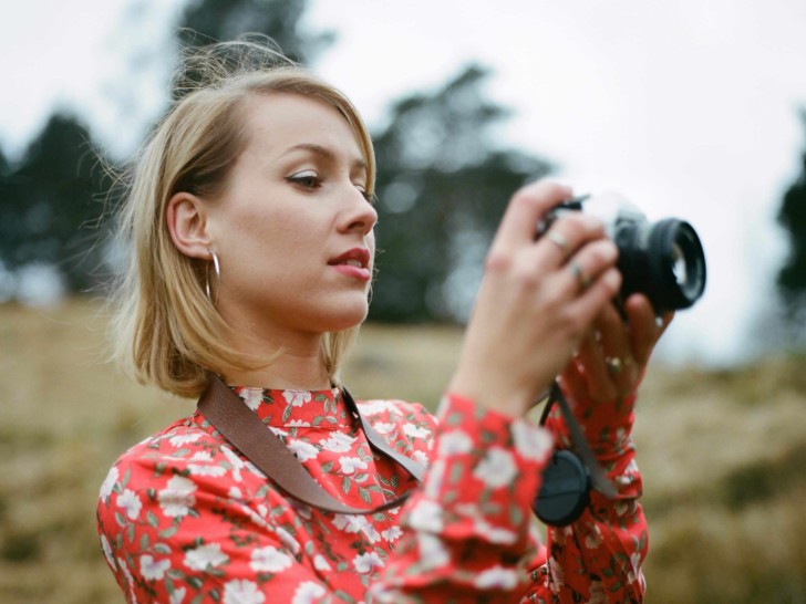 Radka holds a camera. She has blonde hair and wears red lipstick