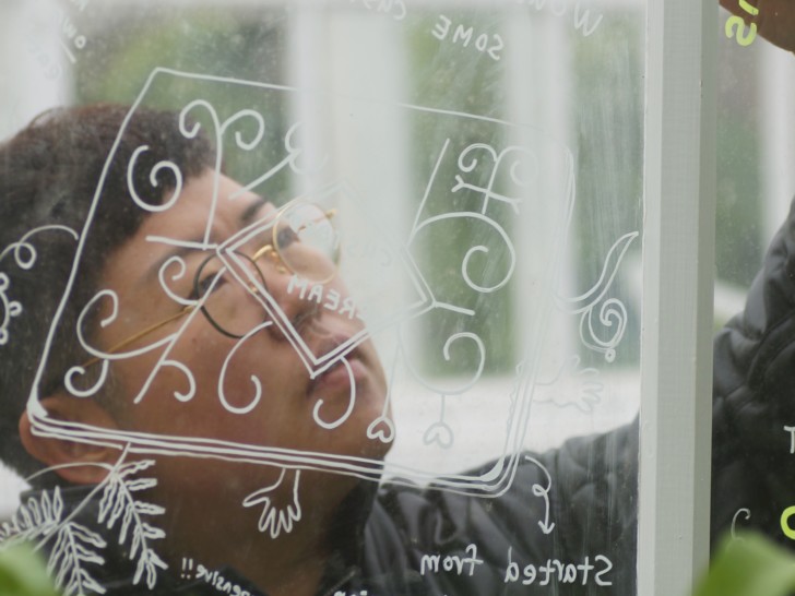 Taey is photographed drawing on a glass pane with white marker, looking very focused.