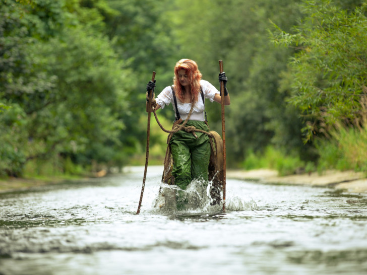 Photograph of Kerry Morrison wading through a river using two large sticks for support