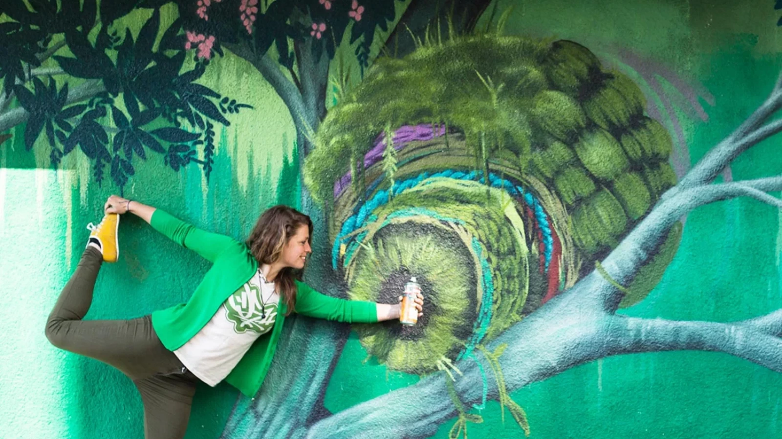 Faunagraphic aka Sarah Yates stands on one leg in front of a mural she painted.