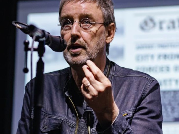 A man with short dark hair and round glasses speaks in to a microphone.