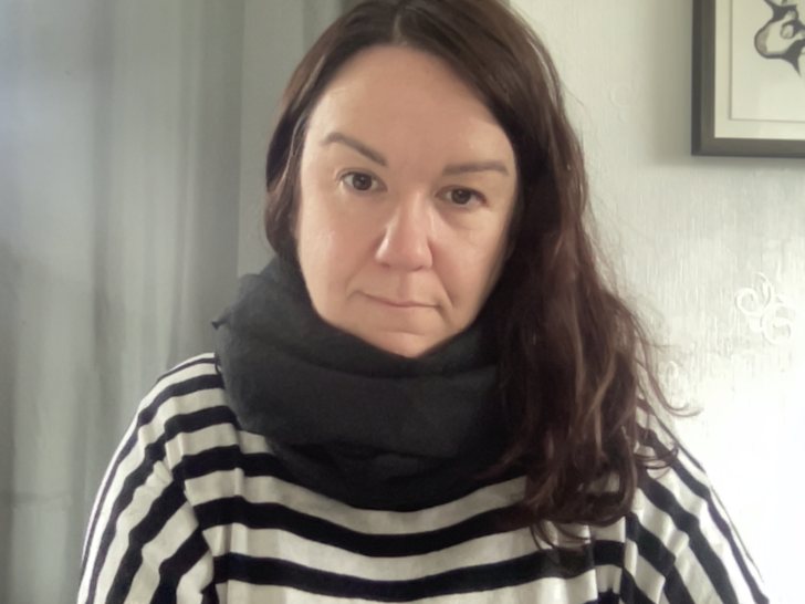 A woman with long brown wearing a black and white stripped top and a dark coloured scarf around their neck.