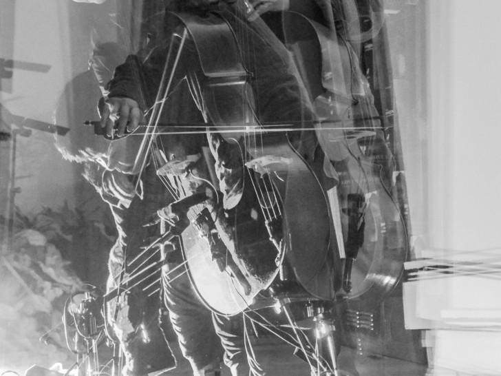 A black and white photograph has been digitally altered, layering over one another multiple images of a person in different poses while playing the cello.