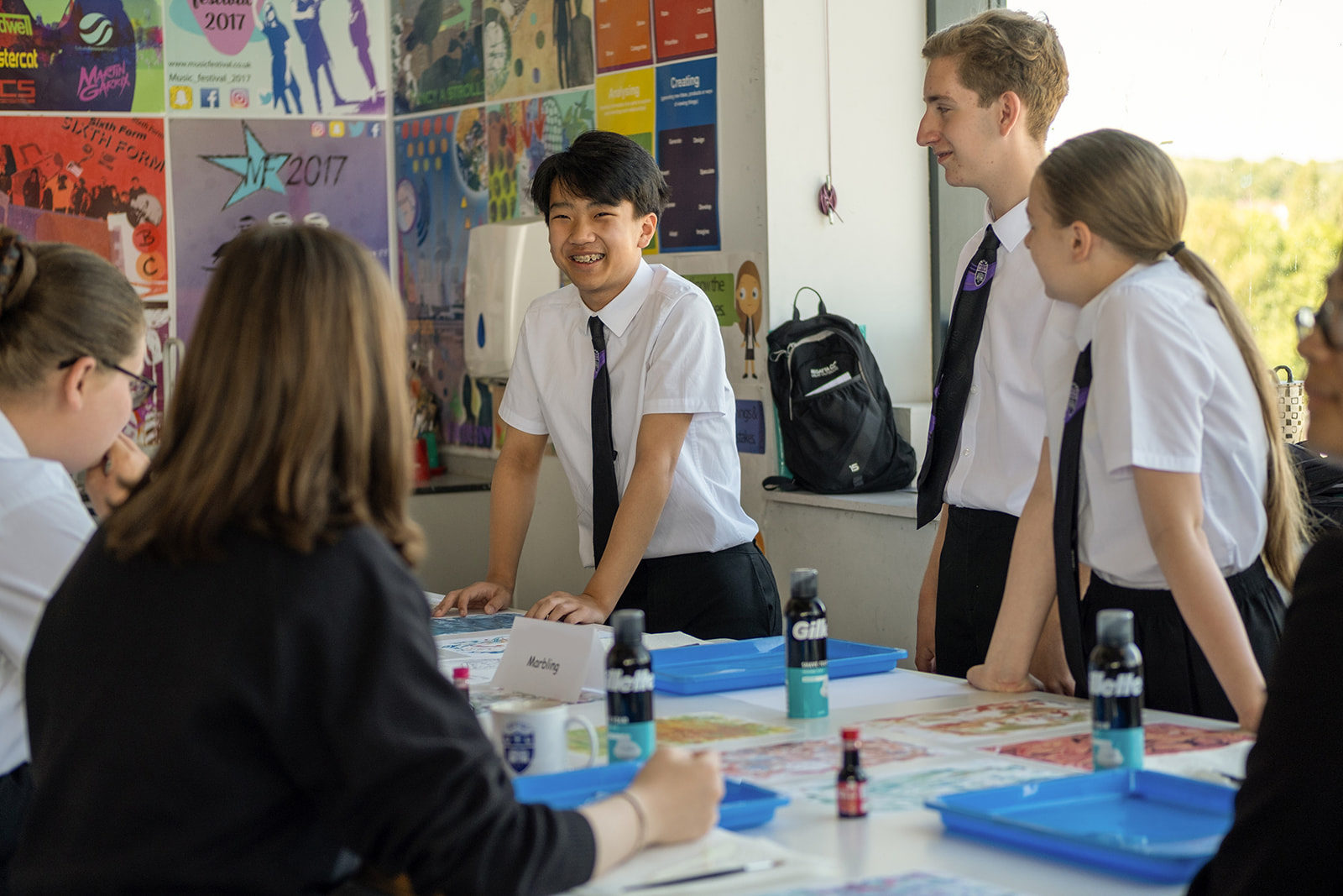 A group of young people in school uniform chat over a table where they are making artwork