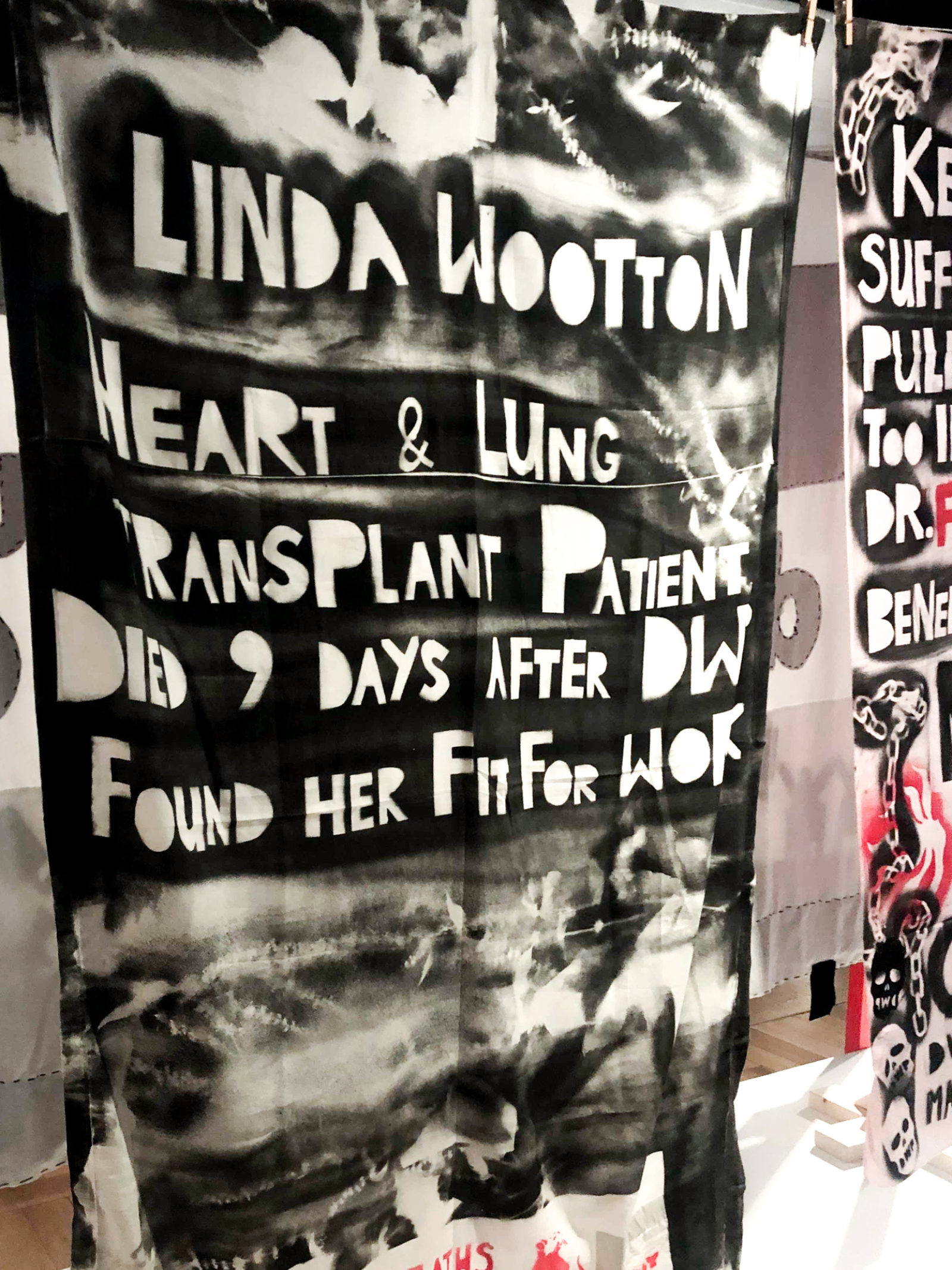 A black and white hand made tapestry reading 'Linda Wooton Heart & Lung transplant patient died 9 days after DWP found her fit for work'.