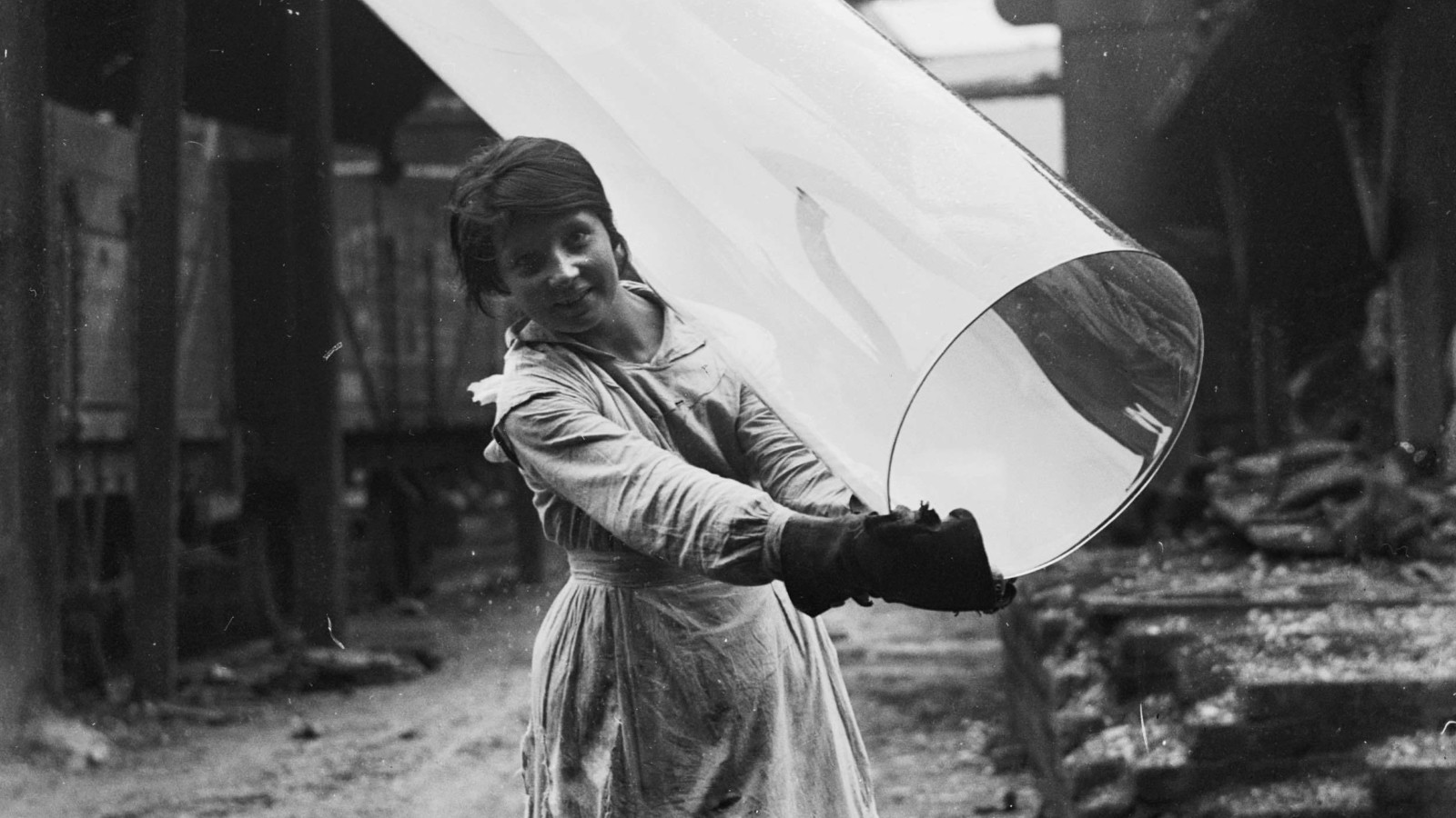A black and white photo of a girl carrying a large glass cylinder.