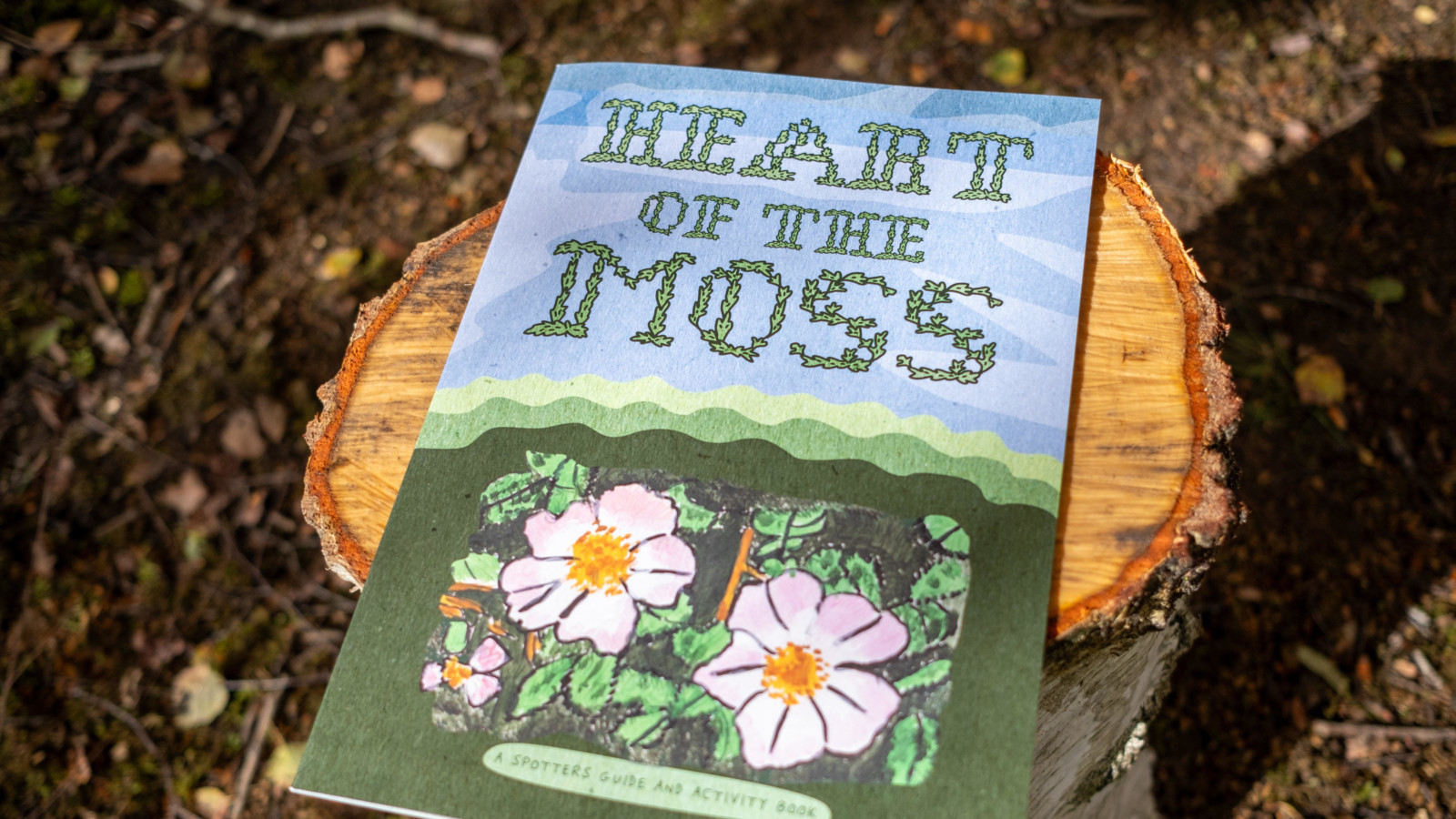 Photograph of an activity book with floral illustrations on the front, entitled Heart of the Moss