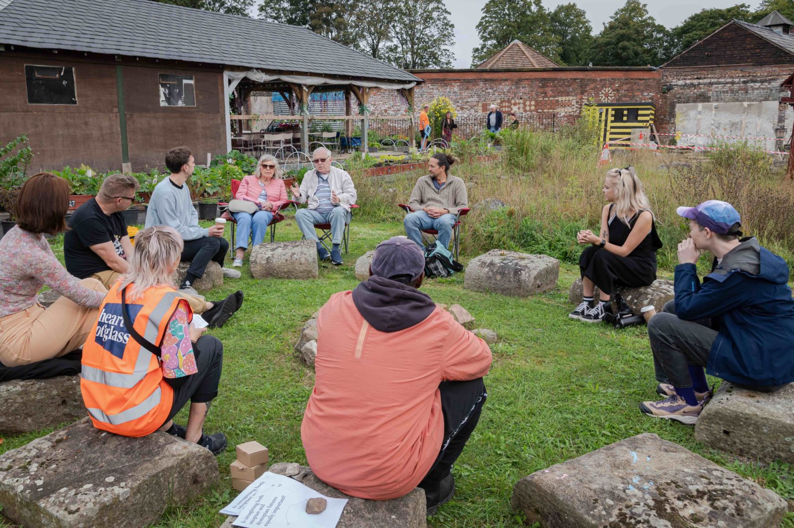 A group of people having a discussions sit on a circle of rocks at incredible edible Knowsley as part of environmental justice questions with Harun Morrison