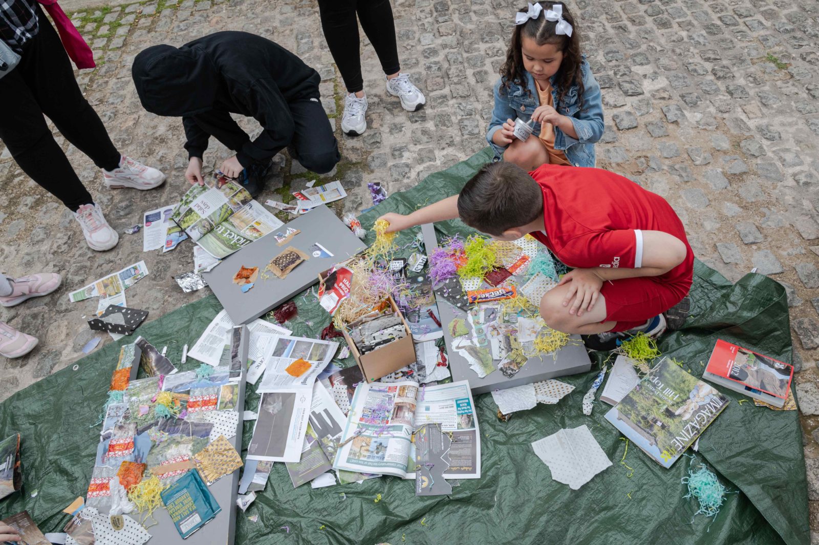 3 kids are doing crafts with recycled materials.