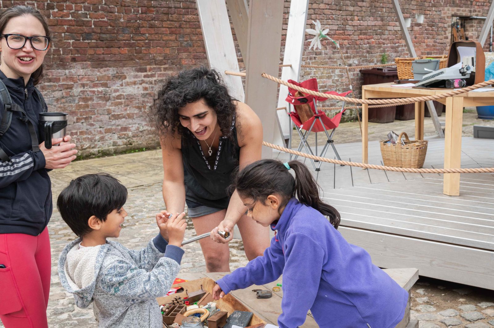 Bea Albanese looks through recycled objects with two young children and their mother, they are all smiling and laughing.