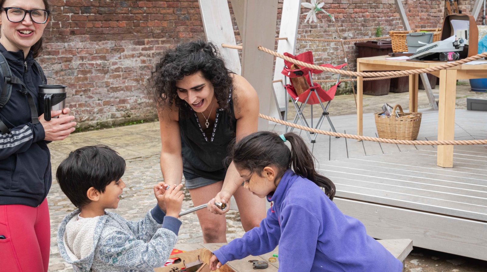 Bea Albanese looks through recycled objects with two young children and their mother, they are all smiling and laughing.