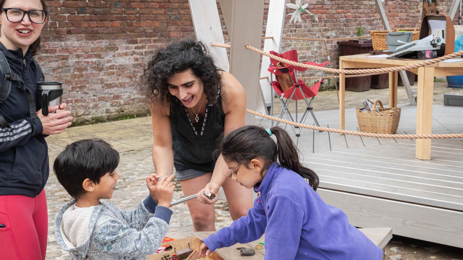 Bea Albanese looks through recycled objects with two young children and their mother, they are all smiling and laughing.