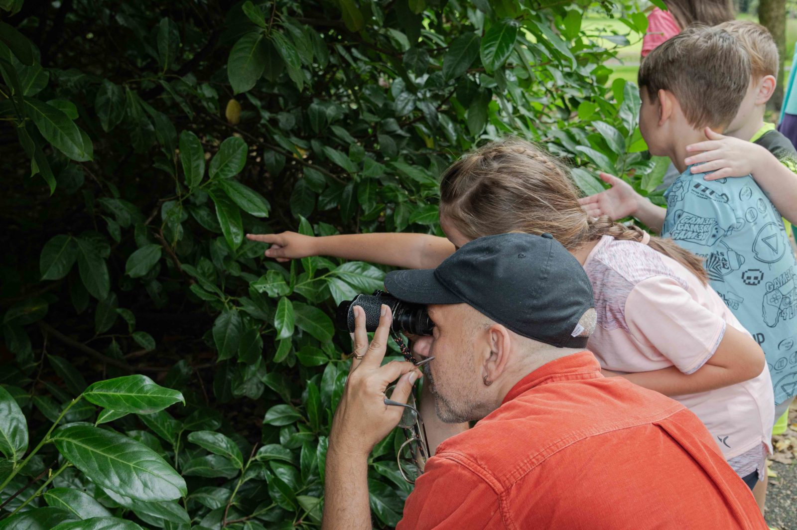 Paul looks into a bush with binoculars. A little girl standing next to him points at something in the bush.