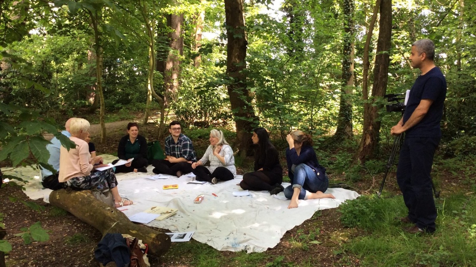 People sit around a blanket in a forest having a discussion.