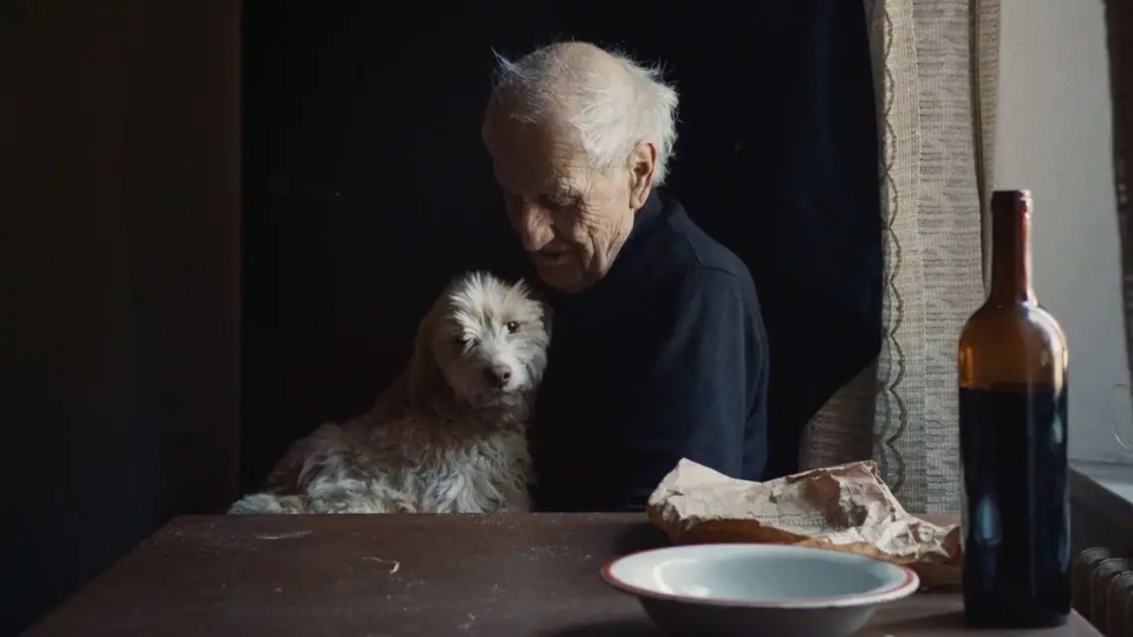 A man is sat at a table with a fluffy dog on his lap.