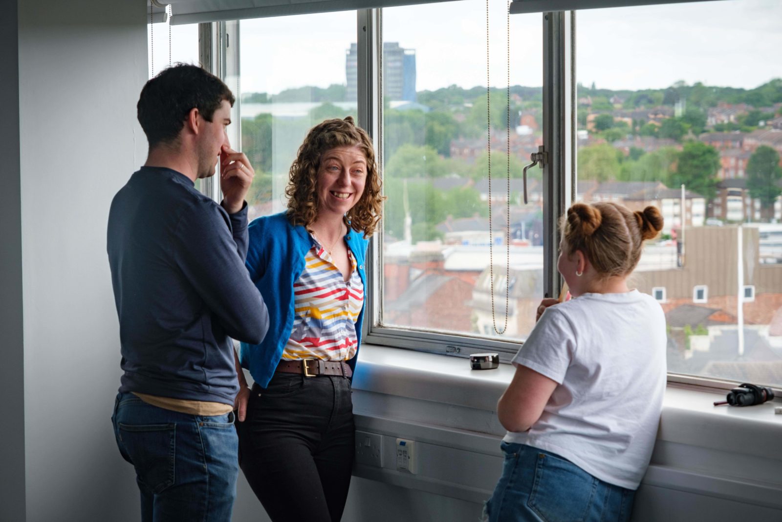 3 people having a conversation in front of the window.