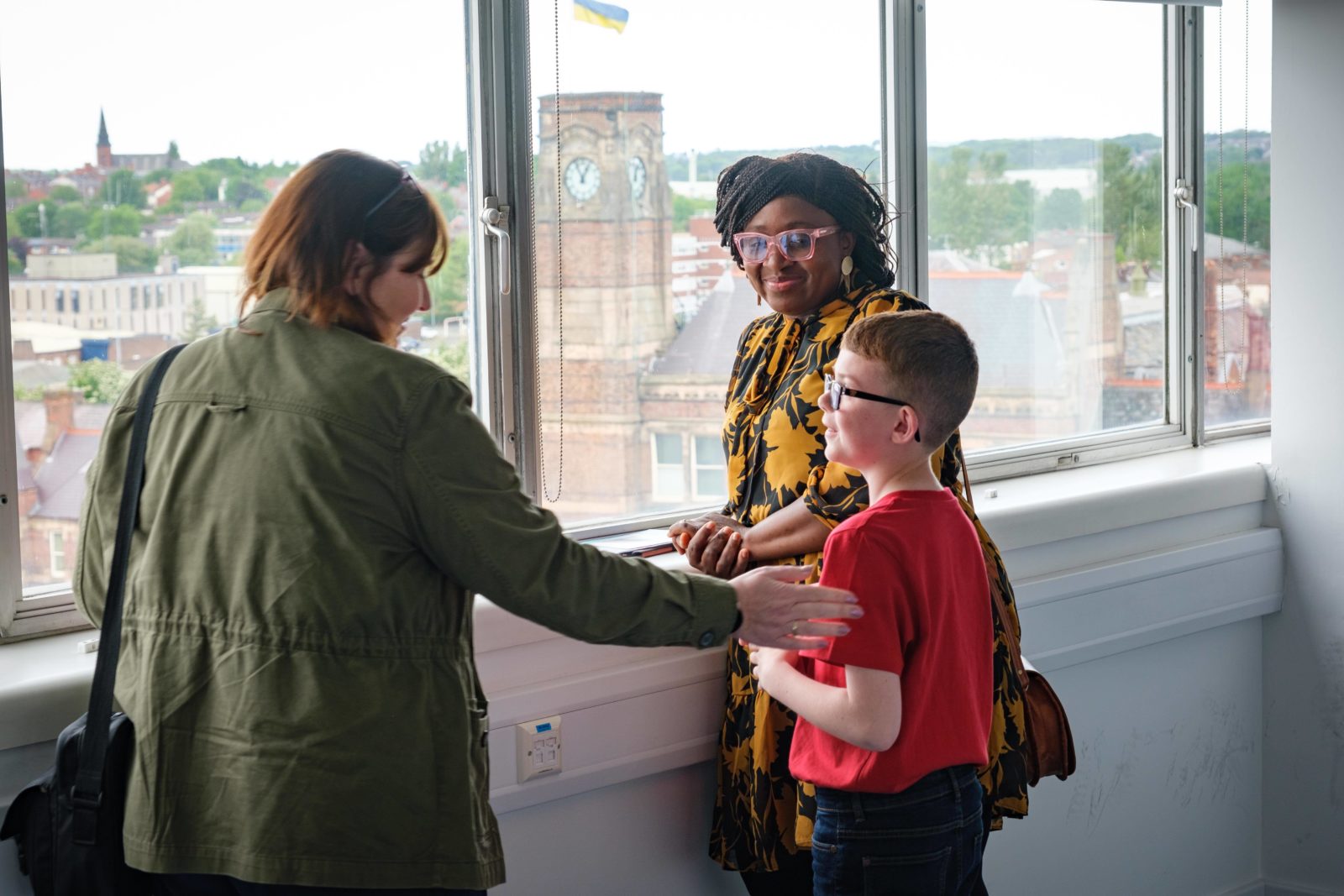 2 women talk to a schoolboy looking out of the windows, one has her hand on his shoulder.