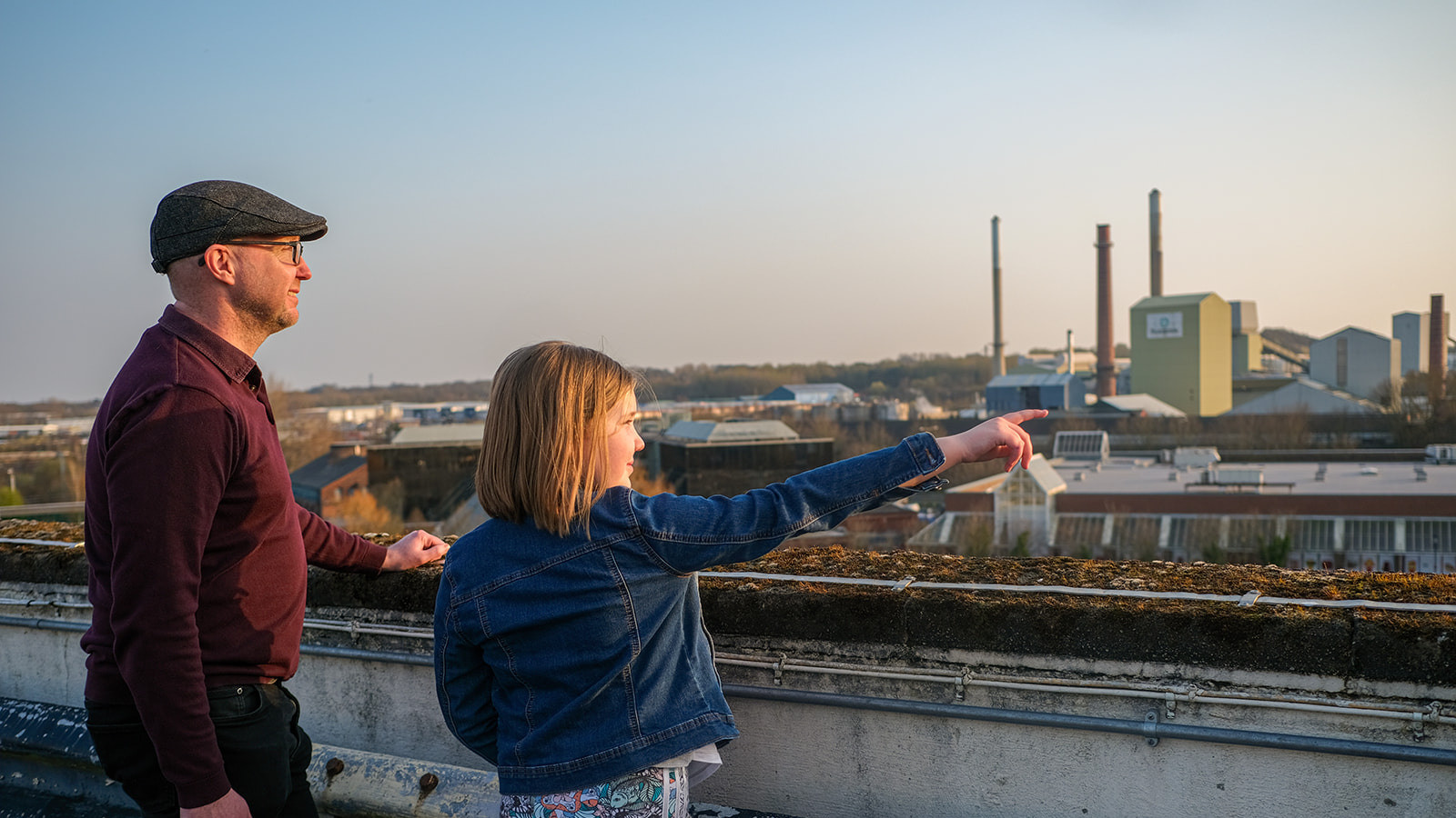 Two people, a child and an adult, stand in the evening light looking out over St Helens. The child is pointing to something in the distance.