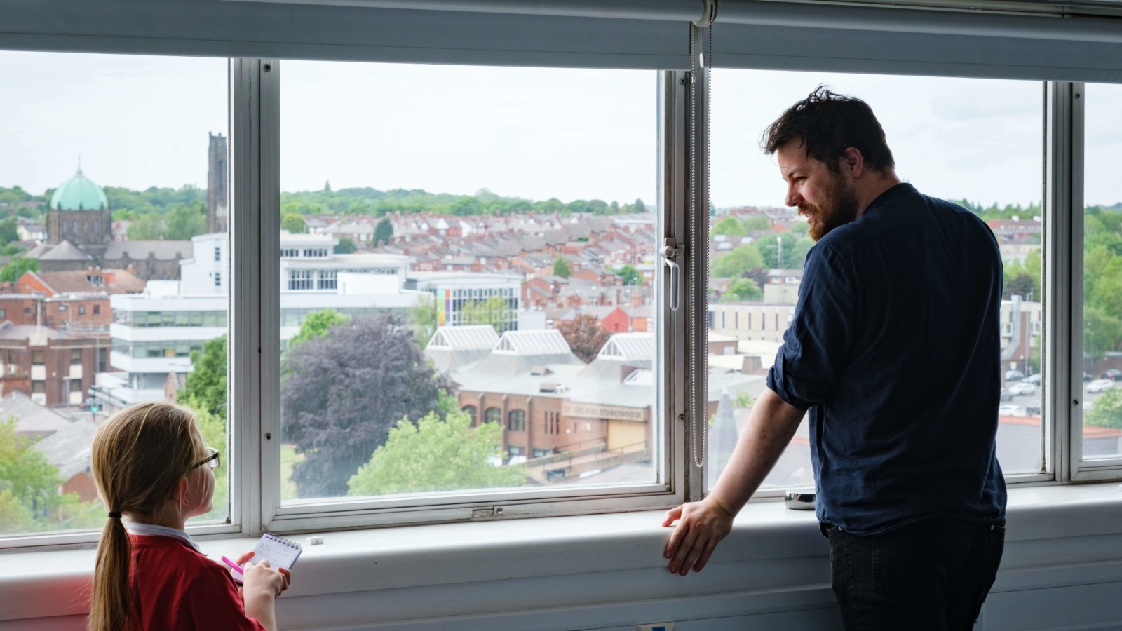 A man and a child talking in front of the windows.