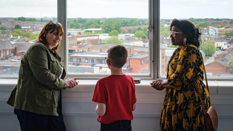 Photograph of 2 women having a conversation with a schoolboy in front of a window that looks over St Helens.
