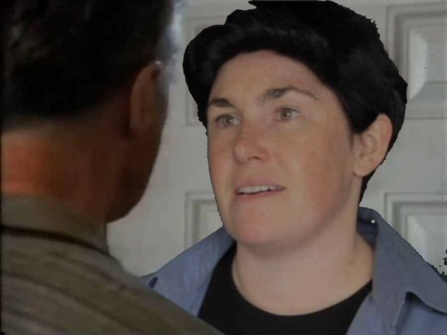 Artist Amy Pennington wears a short, black wig and a blue shirt and is facing a person with short dark hair mid conversation.
