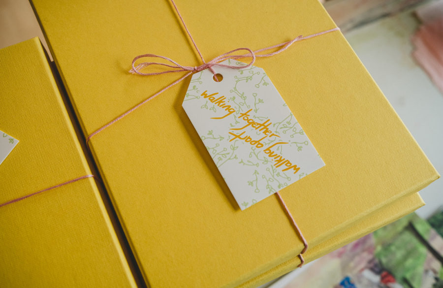 A stack of yellow packages with pink string tied around and a label reading 'walking together, walking apart'.