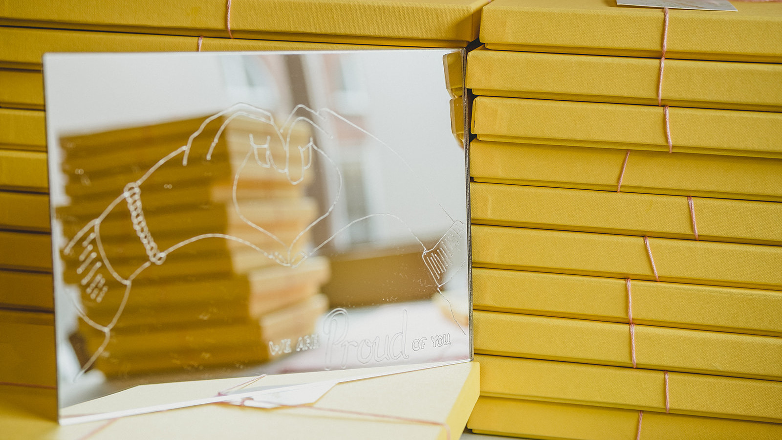 Two stacks of yellow packages with pink string tied around them and a mirror with a white line drawing of two hands making a heart symbol.