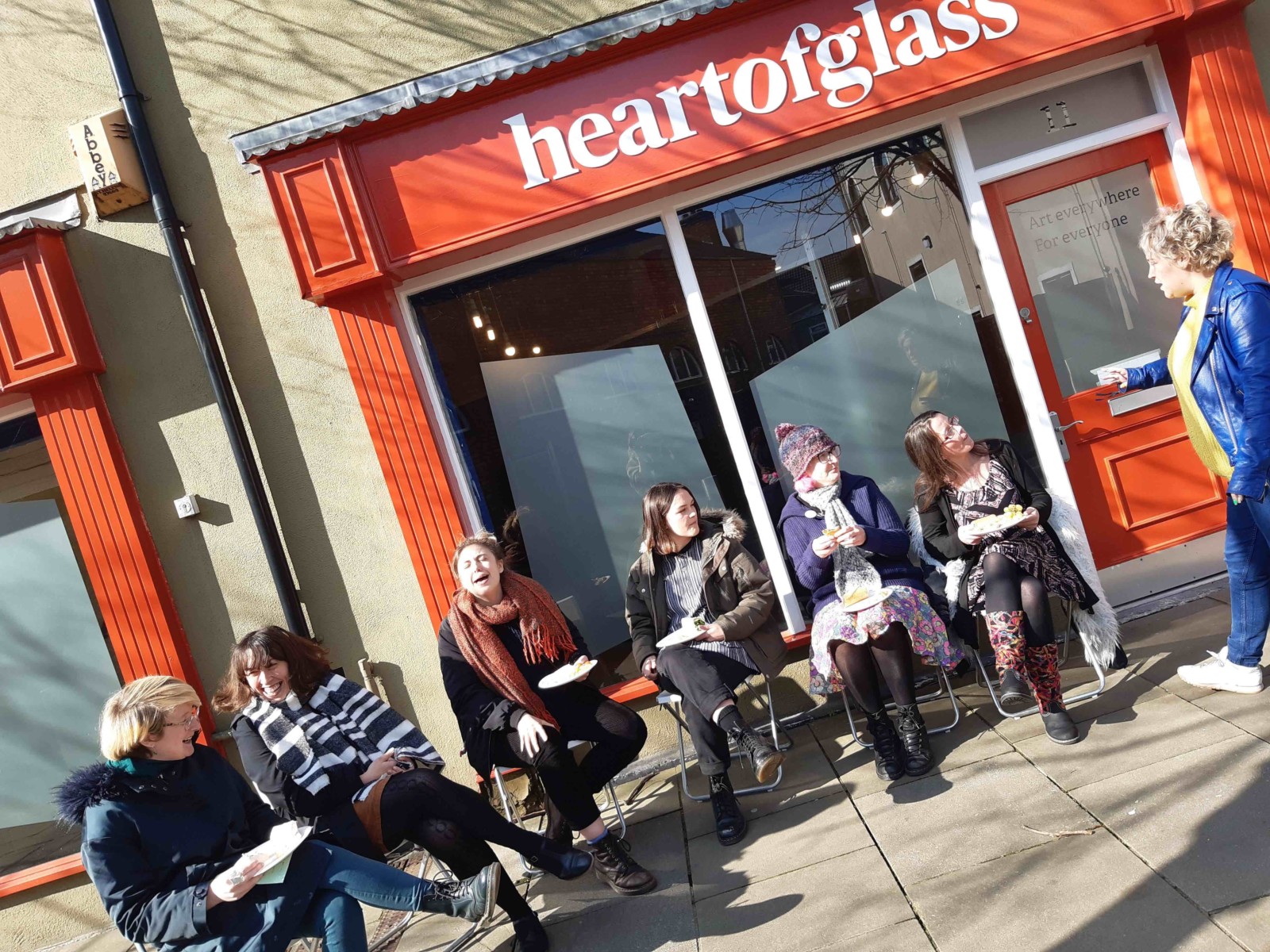 A group of people sit on chairs laughing and chatting in the sun outside the Heart of Glass office.
