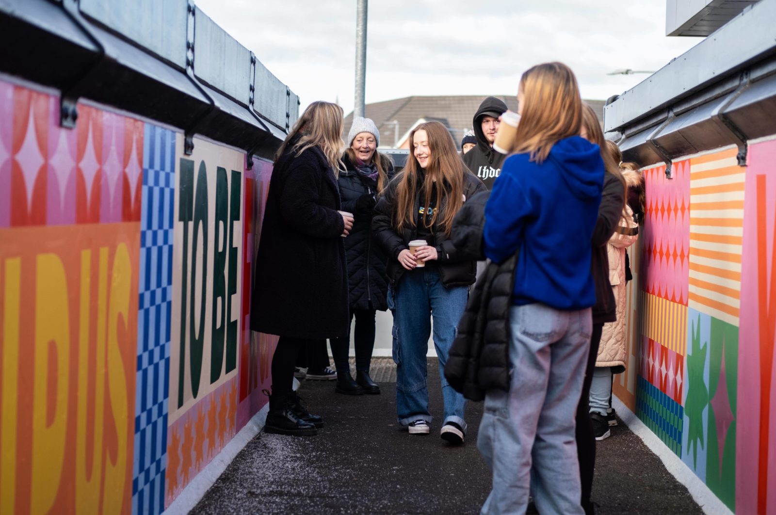A group of people stand on the bridge talking and looking at the colourful mural.