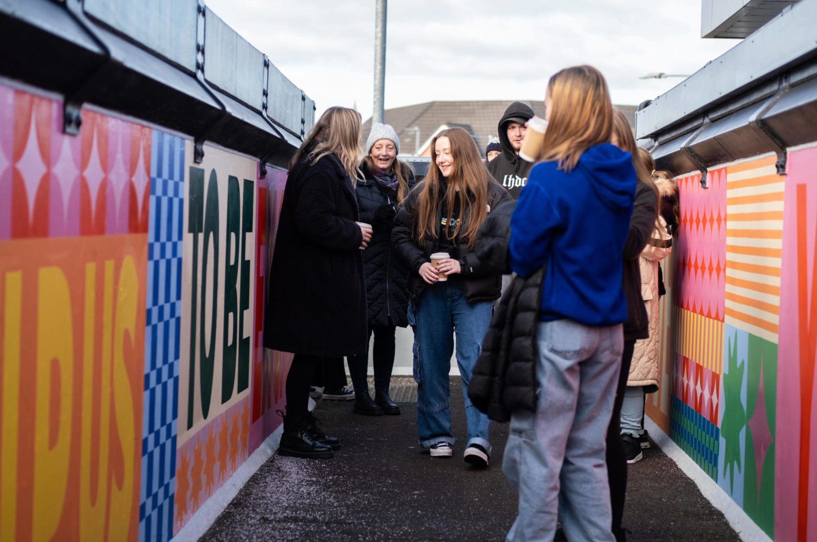 A group of people stand on the bridge talking and looking at the colourful mural.