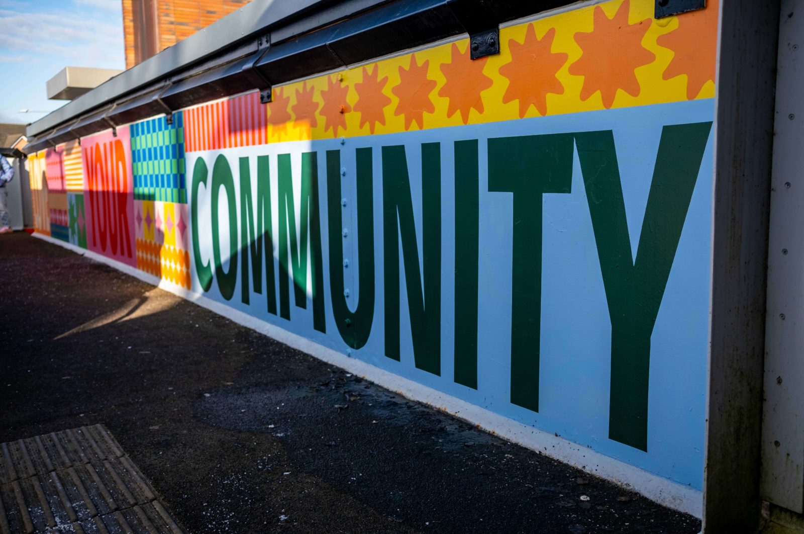The mural is photographed from one side of the bridge, the word 'Community' is in focus.
