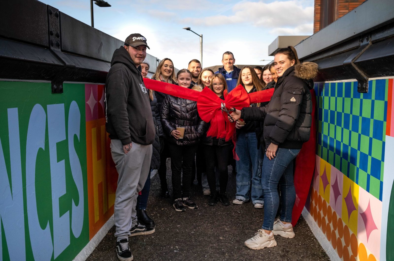 A group of people stand on the bridge, smiling at the camera. They are stood behind a big red ribbon.