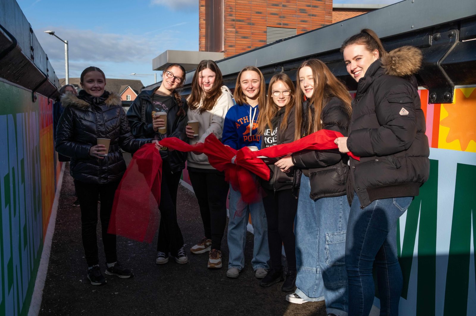 A group of young people smile at the camera holding the ribbon.