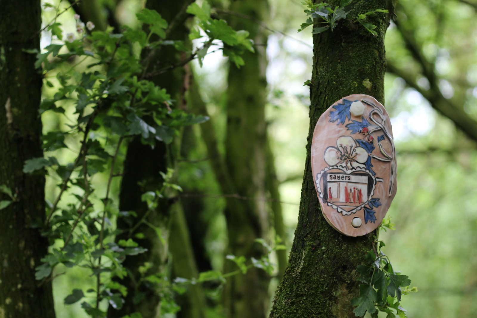 A clay artwork featuring a bakery, a flower and leaves is attached to a tree.