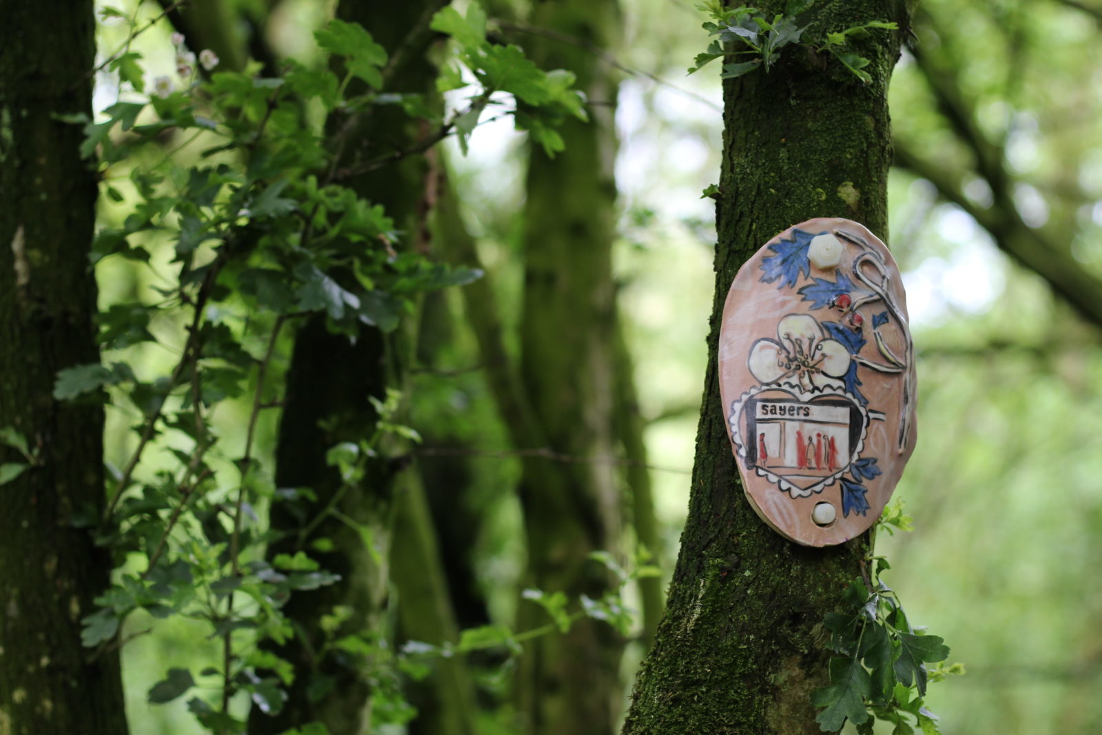 A clay artwork featuring a bakery, a flower and leaves is attached to a tree.