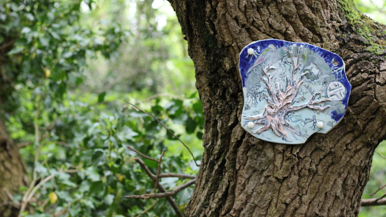 A clay relief featuring a tree is attached to a tree.