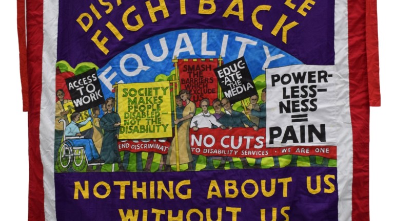 A fabric banner reading 'Disabled People Fight Back ... Nothing about us without us'. In the middle are illustrations of protest signs reading things such as 'Powerlessness = Pain' and 'Society makes people disabled not the disability'.
