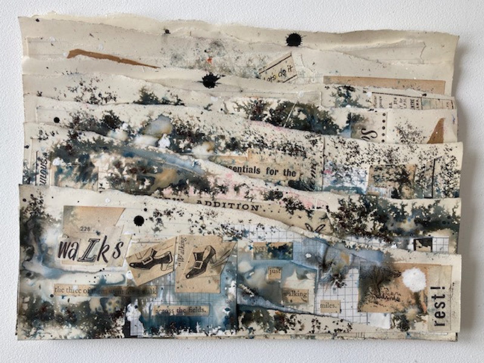 Several pieces of paper that have been torn at different points are layered one in front of the other. They are splashed with ink and collaged with cut out letters and illustrations. The main colours are brown, off white, black grey and blue.