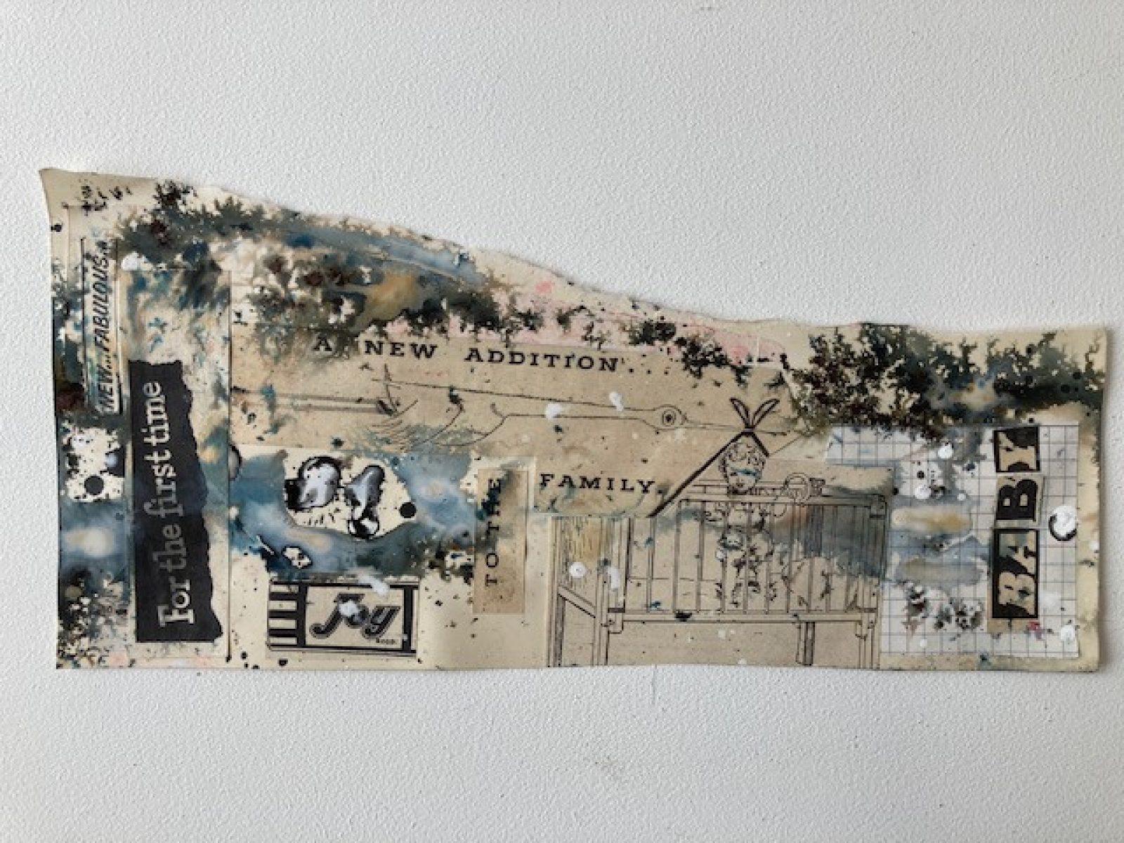A torn piece of off white paper with ink splatters and illustrations and words collaged onto it. Some of the words that can be read say 'For the first time,' and 'new... fabulous' as well as 'baby' and 'new addition to the family'. There is an illustration of a stalk and a baby in a cot.