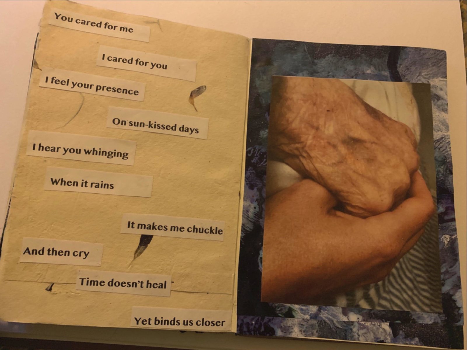 an open sketchbook, on the left hand page the words 'You cared for me I cared for you I feel your presence On sun-kissed days I hear you whinging When it rains It makes me chuckle And then cry Time doesn't heal Yet binds us closer' cut and stuck on what looks like organic or recycled paper. On the right hand page 2 hands are photographed interlocked, one looks like an elderly person's and one looks like a young person's.