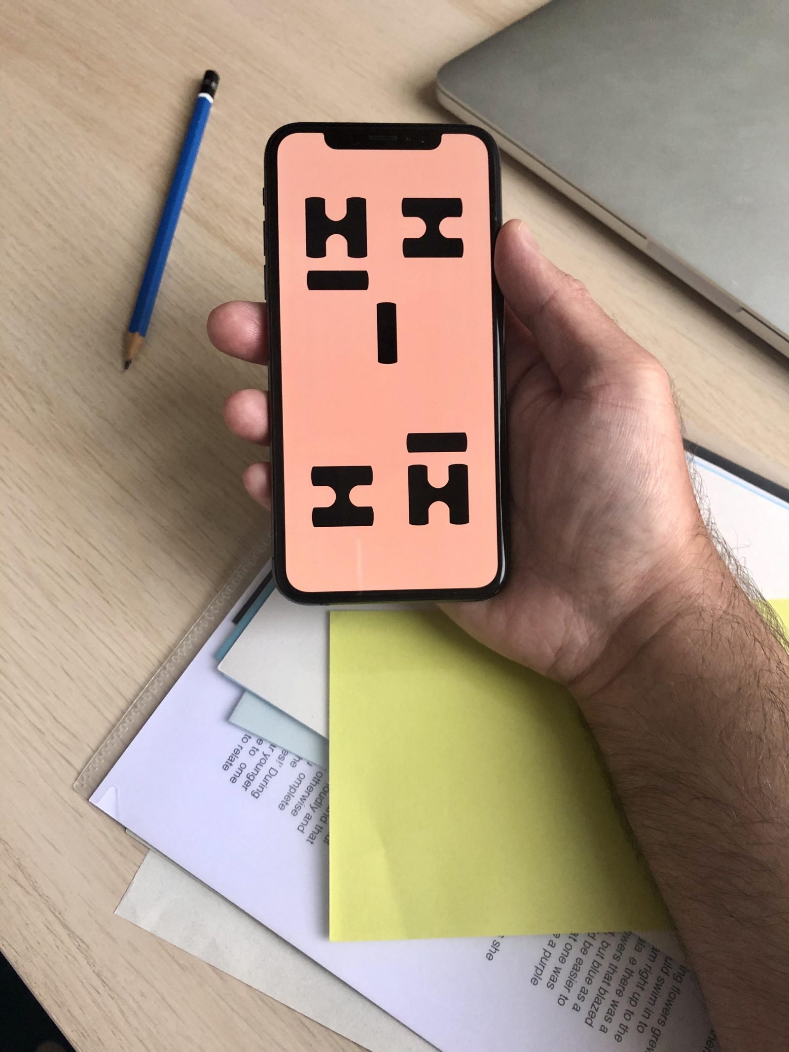 A hand holding a smart phone with an image on the screen of a pattern with pink background and the letters H and I arranged in a pattern.