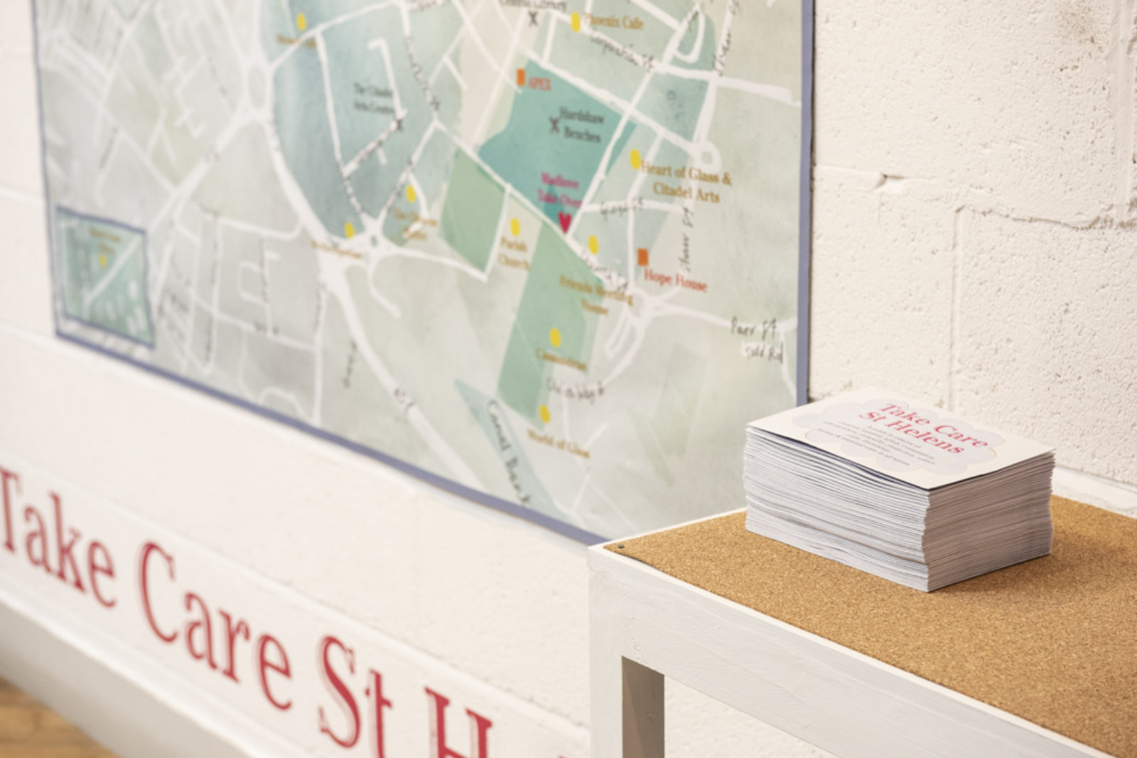 A large scale watercolour painted map hangs on a wall next to a white table. Underneath the map you can see the words 'Take Care St...'