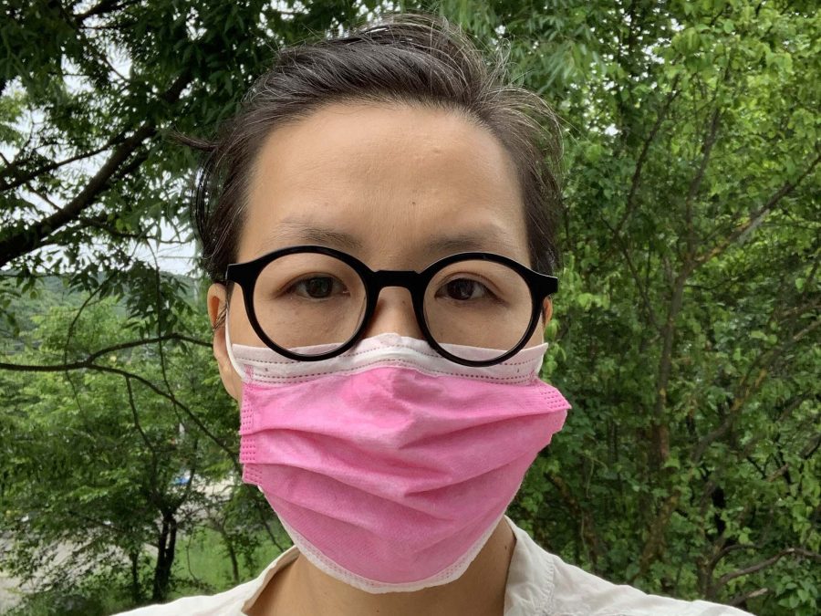 Artist Hwa Young stands against a backdrop of trees. They are wearing a pink medical mask.