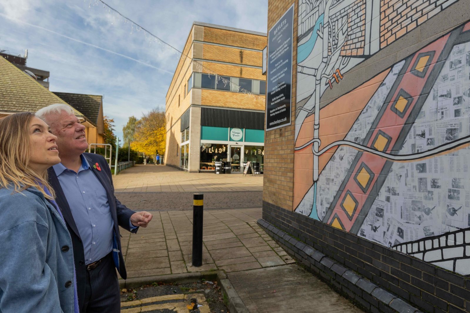 Jo Peel and a man with white hair wearing a suit look up at the mural.