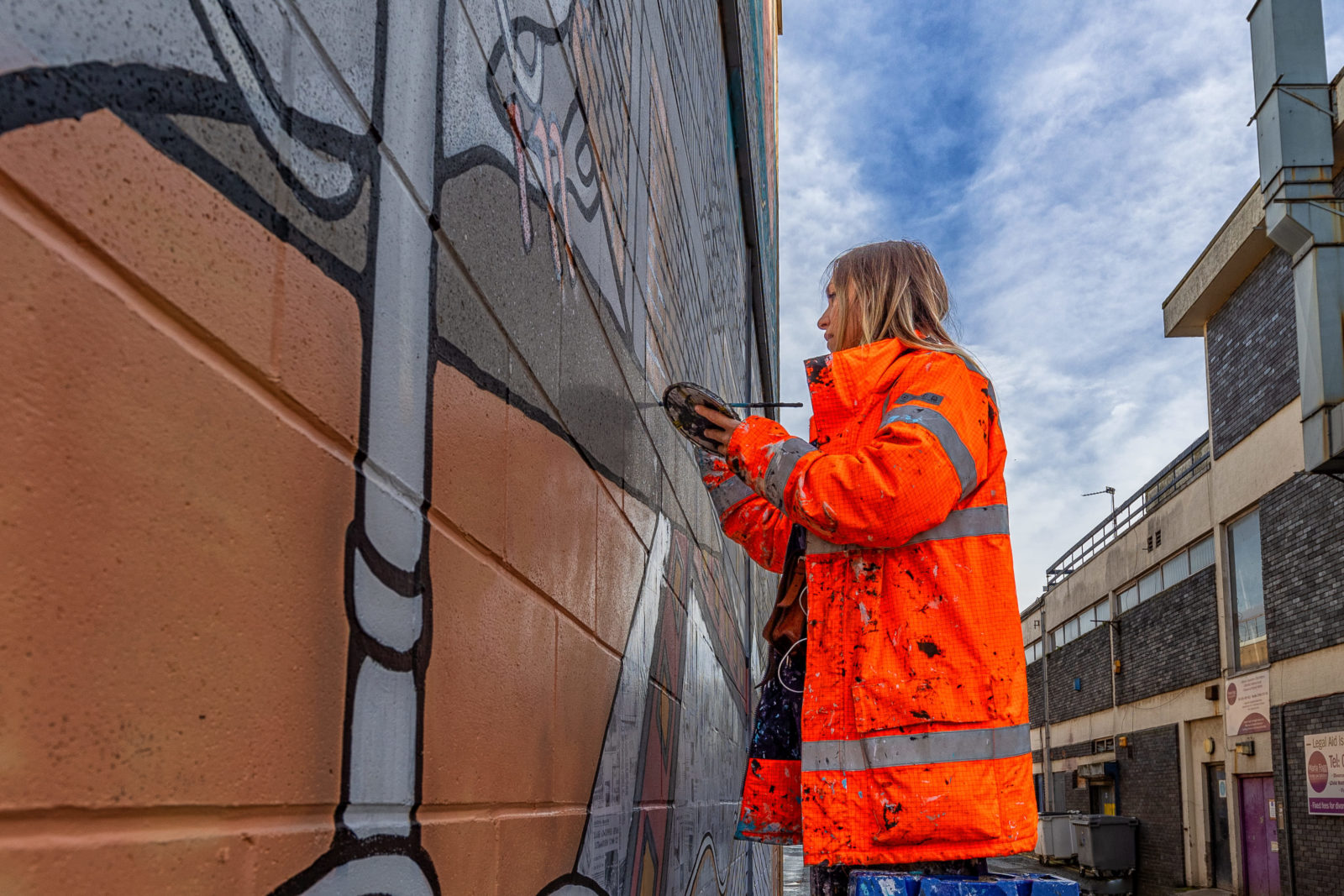 Jo Peel is photographed wearing a hi-vis orange jacket painting the mural.