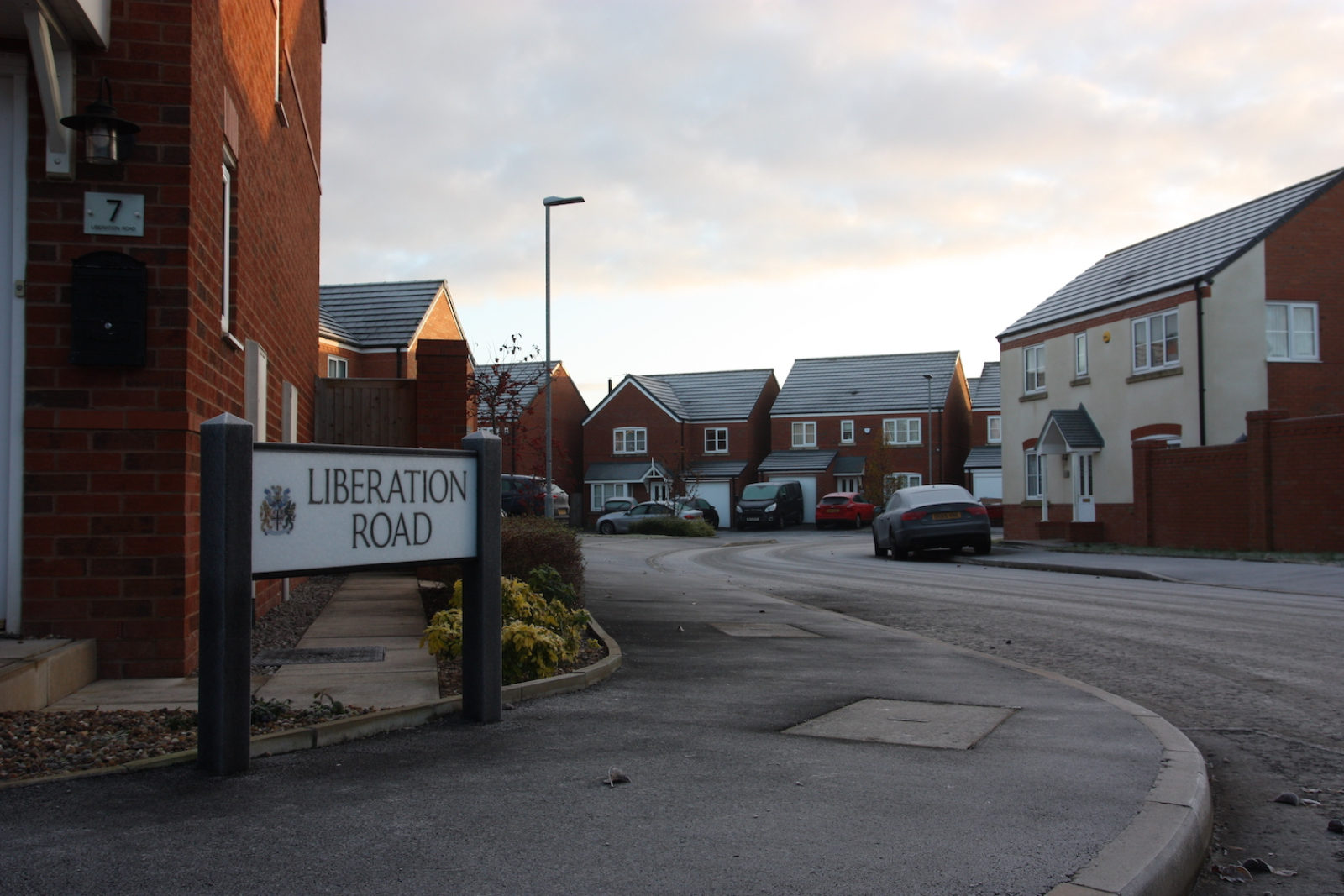 Liberation Road is on the pavement of a winding road which is made up of detached new build houses.
